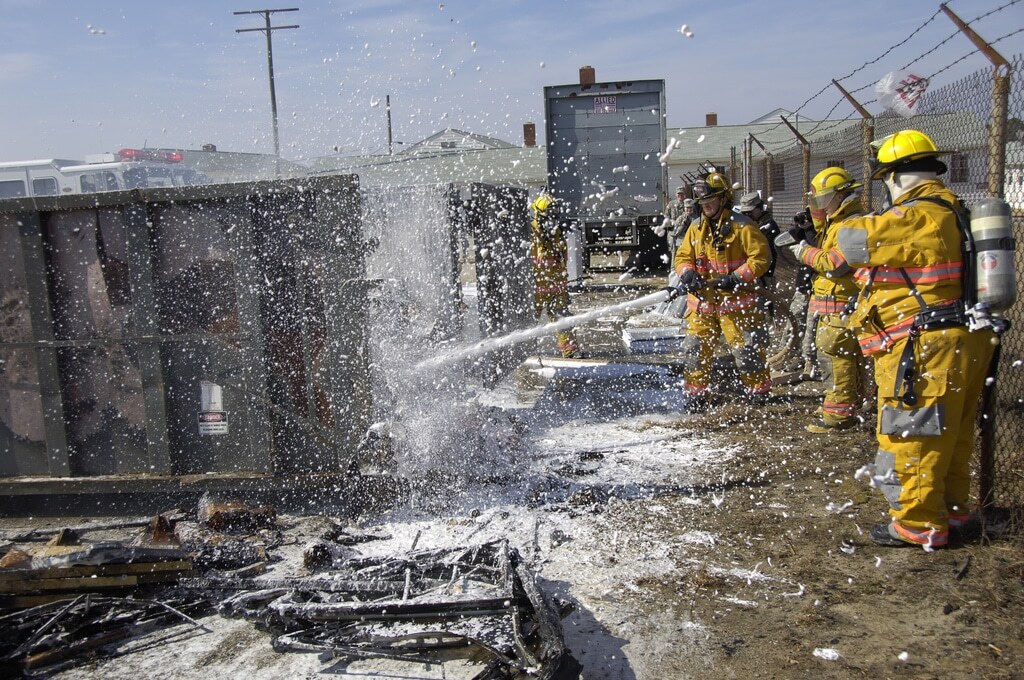 Firefighters hosing down a burned rubbish bin.