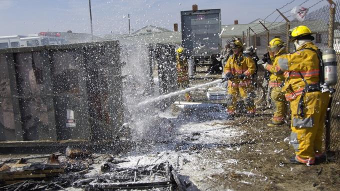 Firefighters hosing down a burned rubbish bin.