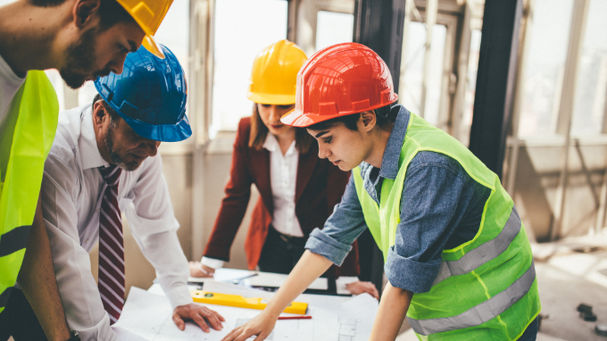 Team of workers hovered over a table discussing project plans.