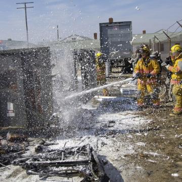 Firefighters hosing down a burned rubbish bin.